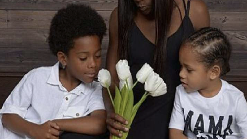 A mother sits with her two young children, gently holding white tulips, symbolizing hope and family connection.