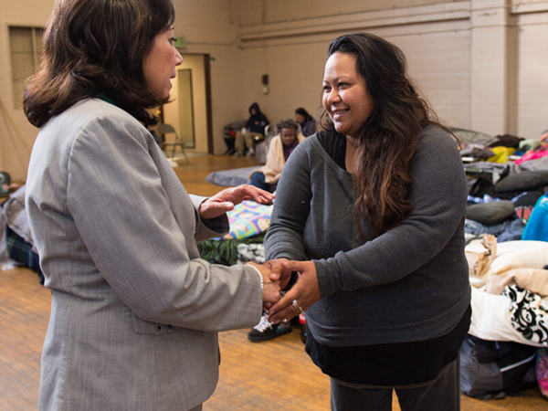 A smiling woman shakes hands with a professional, sharing her journey toward stable housing in a supportive environment.