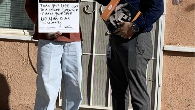 A formerly homeless individual proudly holds a sign with a housing program representative, celebrating their new beginning.
