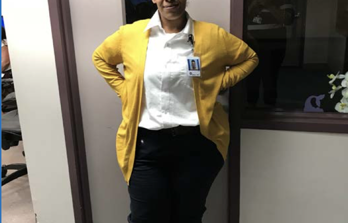A smiling woman in a yellow cardigan stands confidently in an office, embodying hope and resilience in her journey.