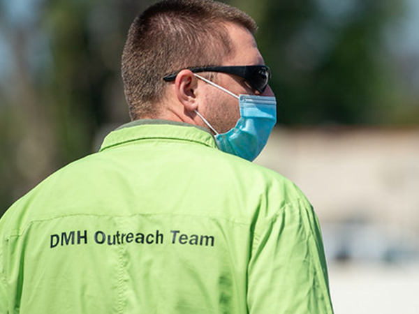 A member of the DMH Outreach Team, wearing a mask, engages with the community to support those experiencing homelessness.