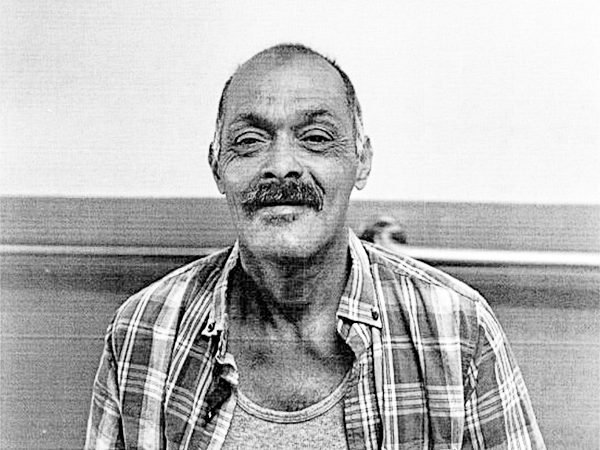 A smiling man in a plaid shirt shares his story of resilience and hope in overcoming homelessness.