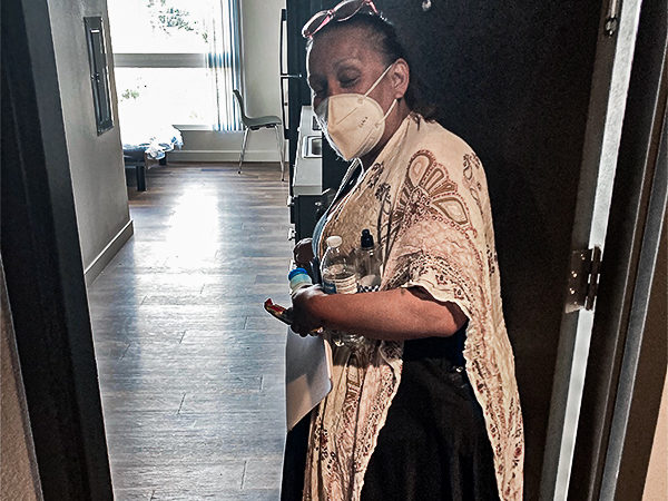 A woman wearing a mask stands at her new apartment door, holding a water bottle, symbolizing hope and new beginnings.