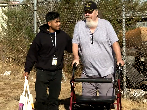 A supportive outreach worker assists a senior man using a walker, highlighting community care and connection in Los Angeles.