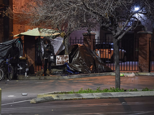 A person stands near a makeshift shelter in an urban area, highlighting the ongoing challenges of homelessness in Los Angeles.