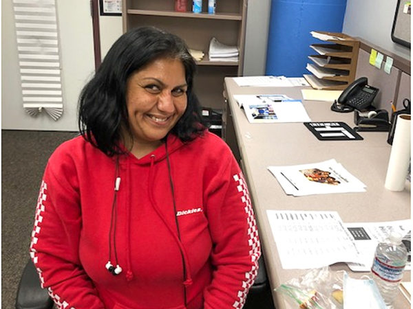 A smiling woman in a red hoodie sits at a desk, representing hope and resilience in her journey toward stable housing.