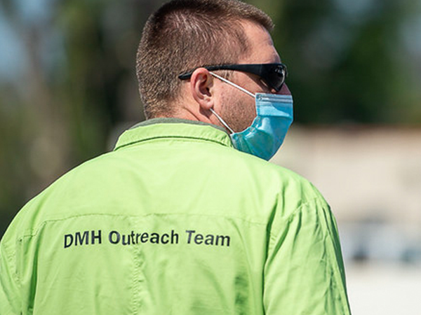 A member of the DMH Outreach Team, wearing a mask, engages with the community to support individuals experiencing homelessness.