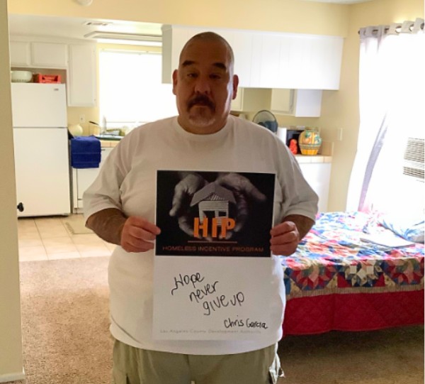 Christopher holds up a motivational sign in his new apartment.