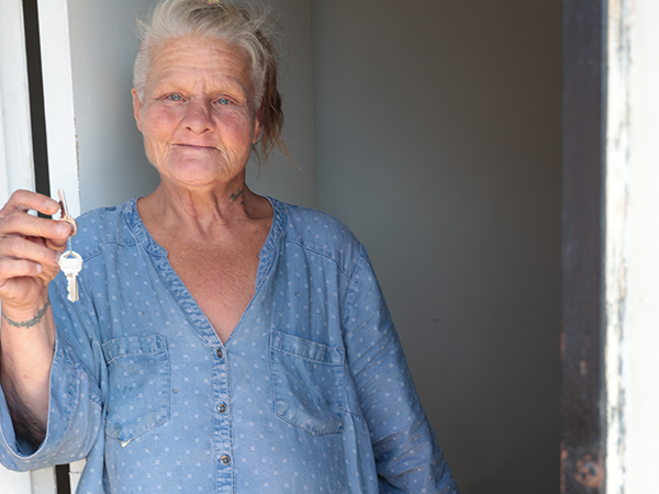A woman holding a key, smiling as she steps into her new home, symbolizing hope and new beginnings.