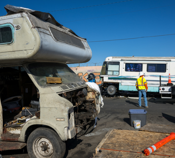 An unoccupied RV, missing pieces, is parking in a lot.