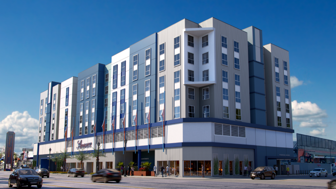 This image shows a contemporary mid-rise building with a sleek, urban design. The structure features: A façade dominated by vertical panels in shades of blue and white, complemented by evenly spaced windows. A central section with a recessed balcony area framed by clean, angular lines. A ground floor that appears to house commercial spaces, with large glass storefronts and signage for "Samaritan" prominently displayed. Multiple flags lining the perimeter of the building, adding a formal or institutional touch. Surrounding elements like parked cars, pedestrians, and a busy street, suggesting the building is situated in a bustling urban environment. The design reflects functionality and modern aesthetics, likely serving as a mixed-use or residential facility with community-oriented features.