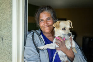A woman stands in the doorway of her new apartment, holding her pet dog.