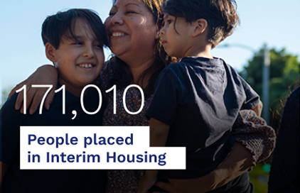 A joyful mother holds her two children, celebrating their placement in interim housing, reflecting hope and community support.