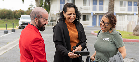 Three individuals engage in a supportive conversation, sharing resources and smiles outside a housing facility in Los Angeles.