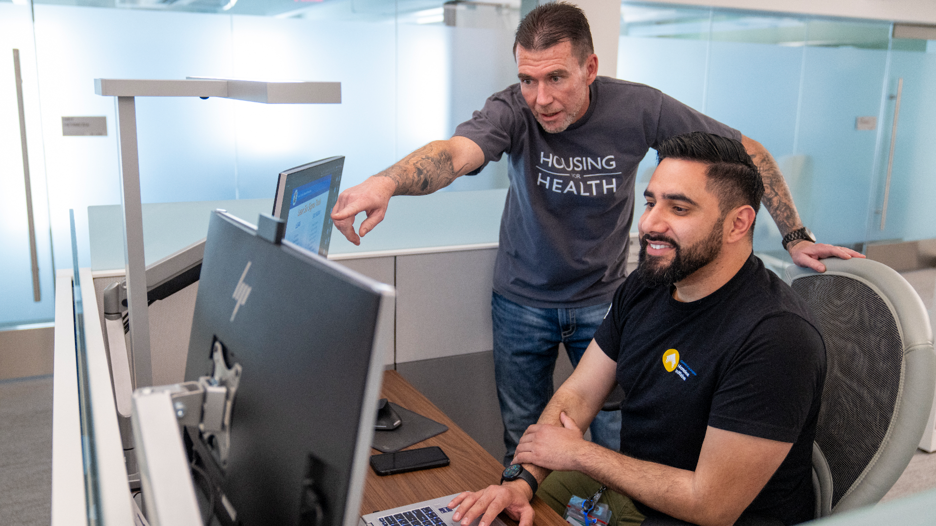 Two men collaborate at a computer, discussing housing resources and support services to aid those experiencing homelessness.