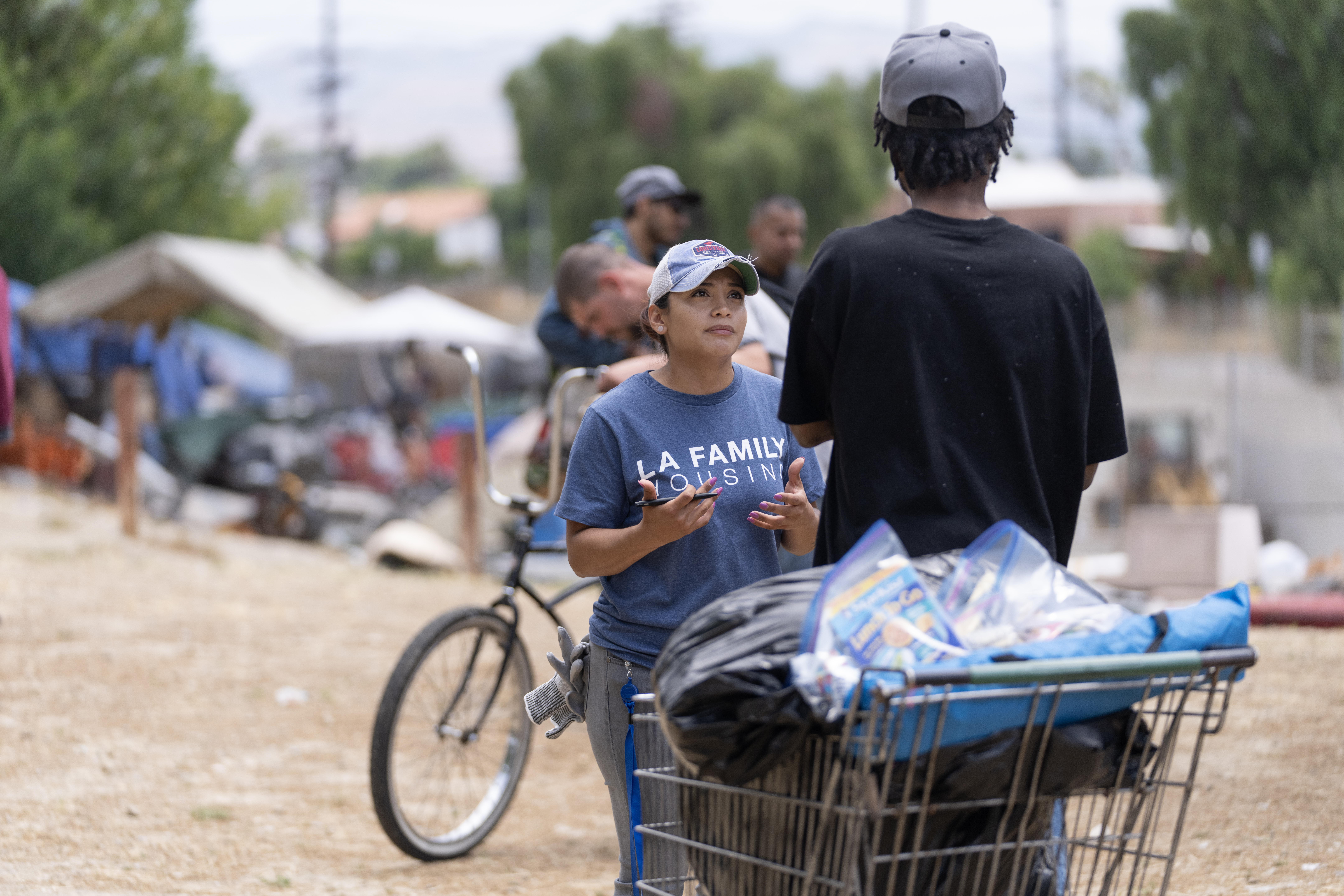 An outreach worker speaks with a man wearing a black shirt and grey hat.