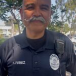 A man with a grey mustache and wearing a badge smiles facing the camera.